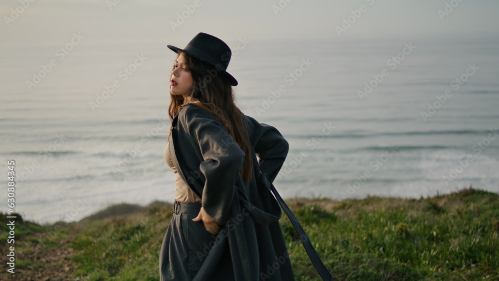 Stylish girl looking sunset standing on green hill near ocean. Model posing Stylish girl looking sunset standing on green hill near ocean. Model posing