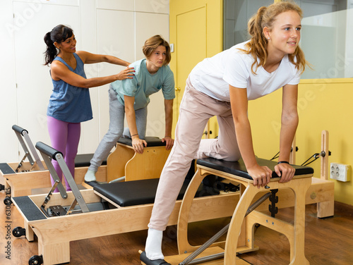 Teenager boy and girl exercising with pilates trainer latin woman in gym. They're training with pilates reformers. © JackF