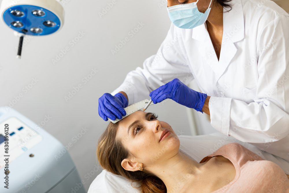 Naklejka premium Woman cosmetologist and female client examining face skin with marker before cosmetology beauty treatment at esthetic clinic