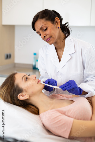Portrait of woman doctor using white pencil for marking place for filler injections on face of patient at beauty clinic