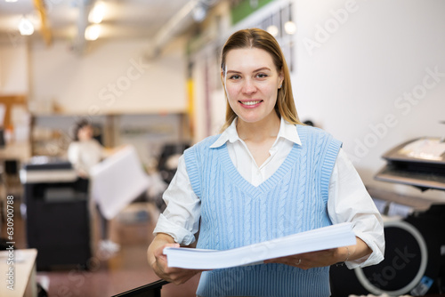 Portrait of positive woman printing office worker with ream of paper.