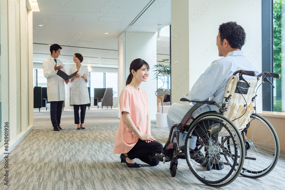 病院で車椅子に乗った患者と会話をする看護師 病院で車椅子に乗った患者と会話をする看護師