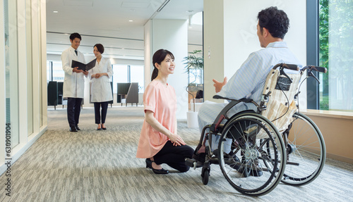病院で車椅子に乗った患者と会話をする看護師 © taka