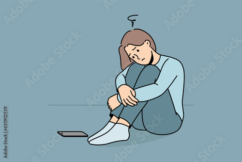 Sad woman is waiting for phone call, sitting on floor and suffering from loneliness or lack of friends. Sad girl sadly awaits arrival of sms message about replenishing bank account