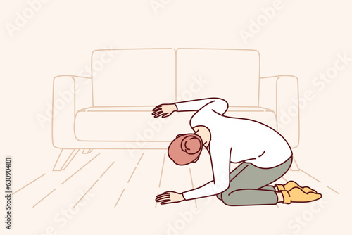 Woman looks under sofa in living room in search of lost wallet with money or missing keys. Confused girl in casual clothes bends down and seeks for TV remote control that fell under sofa