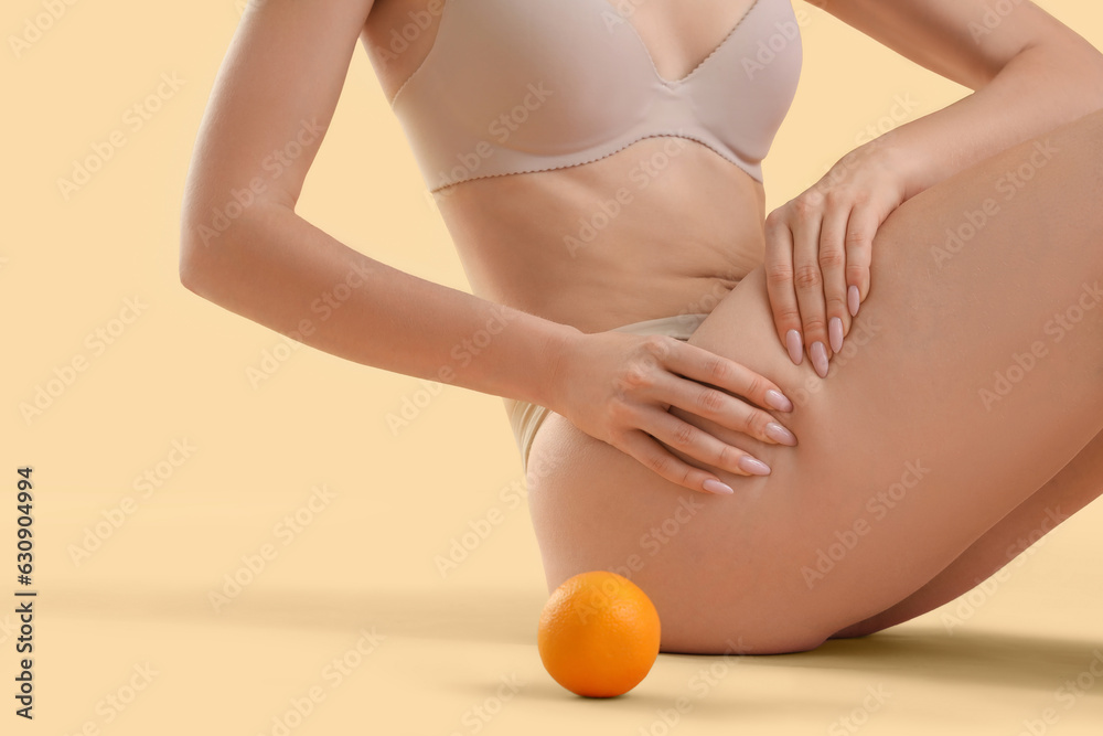 Young woman with cellulite problem and orange sitting on beige background, closeup - obrazy, fototapety, plakaty 