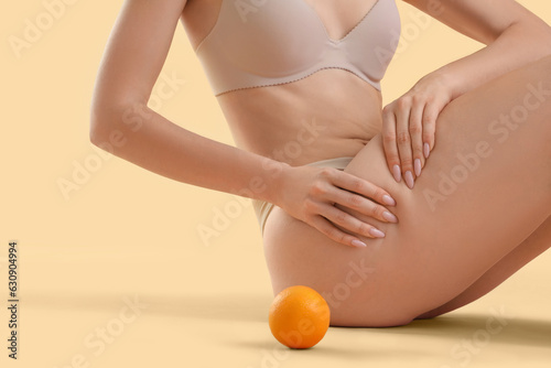 Young woman with cellulite problem and orange sitting on beige background, closeup