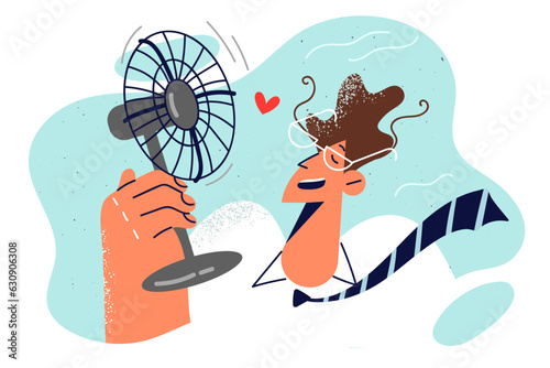 Man with electric fan in hand is trying to freshen up after returning from street in hot weather