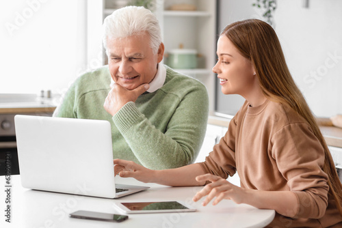 Senior man with his granddaughter using laptop in kitchen