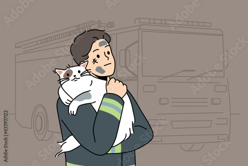 Man firefighter with cat heroically rescued from burning house stands near fire truck and hugs pet. Brave guy in uniform of firefighter or rescue worker helped cat get out of trouble