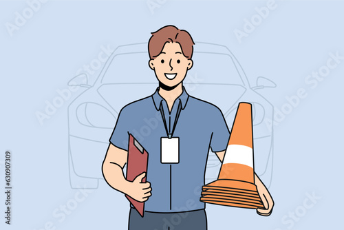 Man instructor from driving school smiles and holds traffic cones inviting to take exam for driver license. Guy employee of car school advertises services company teaching driving.