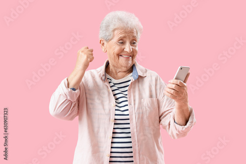Happy senior woman using mobile phone on pink background © Pixel-Shot