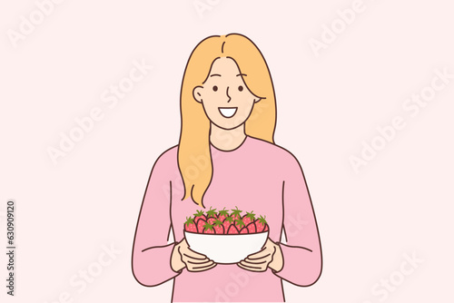 Woman holds plate of strawberries and smiles  offers to try fresh berries and farm fruits