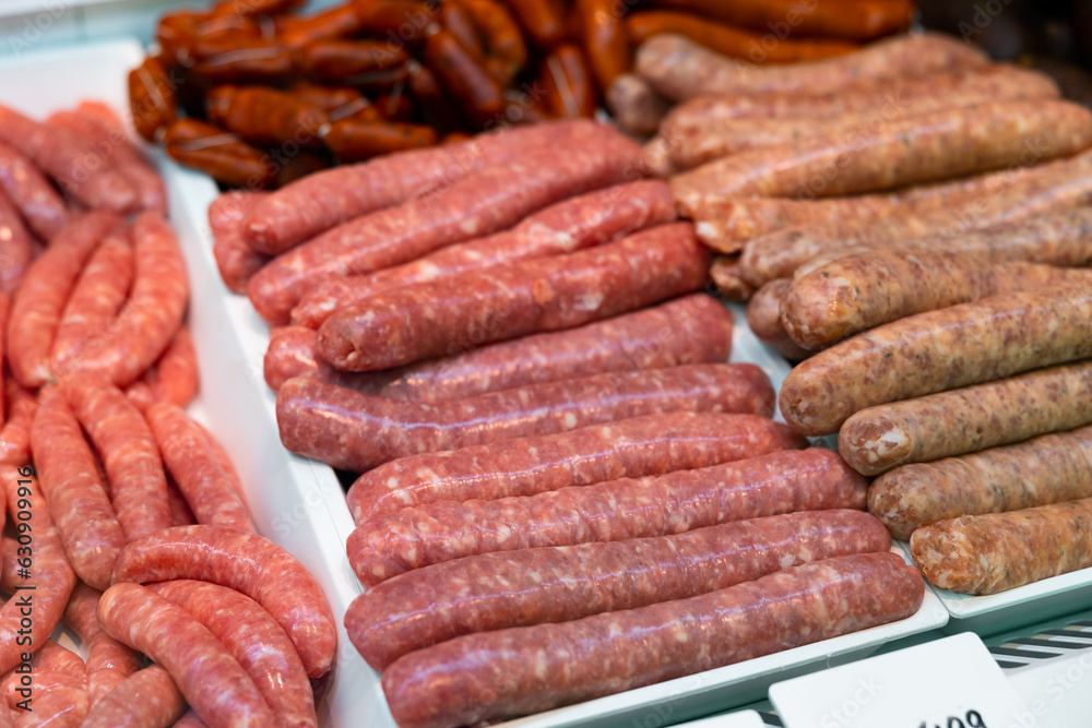 Raw pork-beef sausages in packing tray on glass window refrigerator of butcher shop. Fresh sausages ready for barbecue