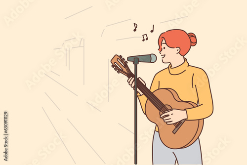 Woman street musician plays guitar and sings standing on sidewalk with microphone
