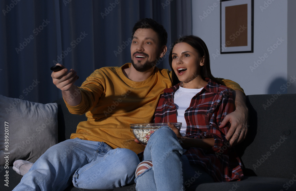 Couple watching TV at home in evening. Man changing channels with remote control Couple watching TV at home in evening. Man changing channels with remote control