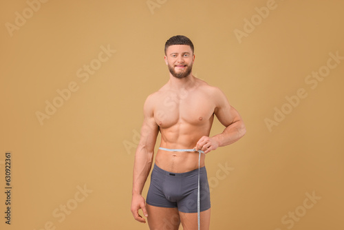 Athletic man measuring waist with tape on brown background. Weight loss concept