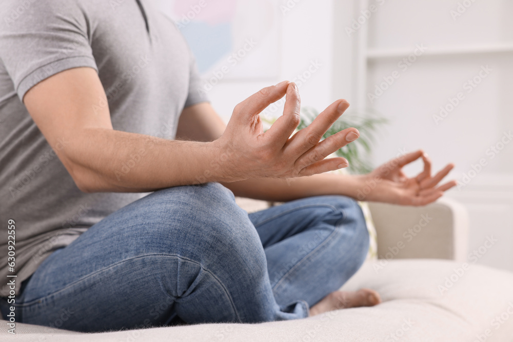 Fototapeta premium Man meditating on sofa at home, closeup. Harmony and zen