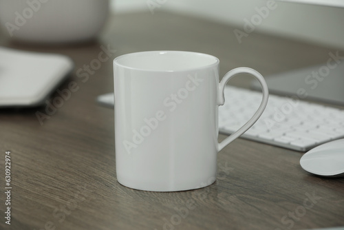 White ceramic mug on wooden table at workplace. Mockup for design