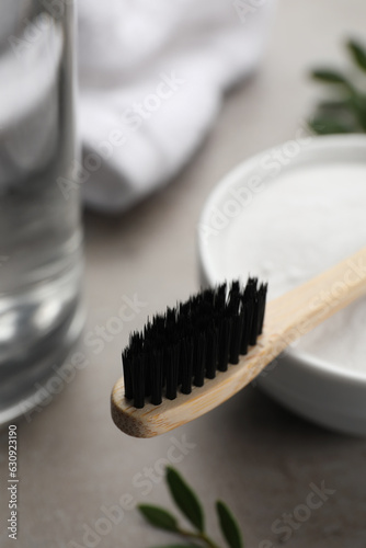Bamboo toothbrush and bowl of baking soda on grey table  closeup