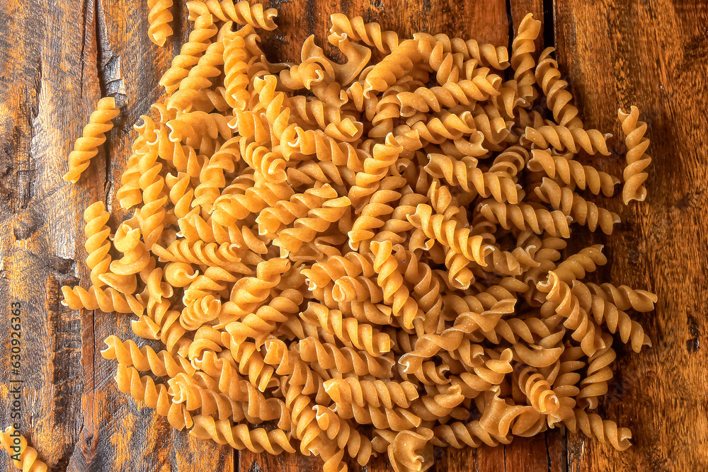 Raw whole grain fusilli pasta on rustic wooden kitchen table Raw whole grain fusilli pasta on rustic wooden kitchen table