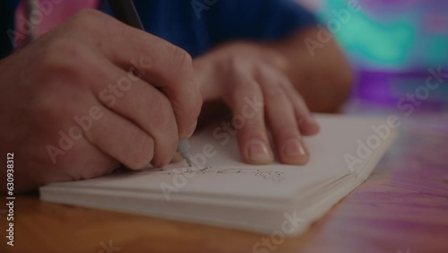 Hands of male artist drawing sketch on paper page in a sketchbook, working at desk in studio. Close-up impersonal shot