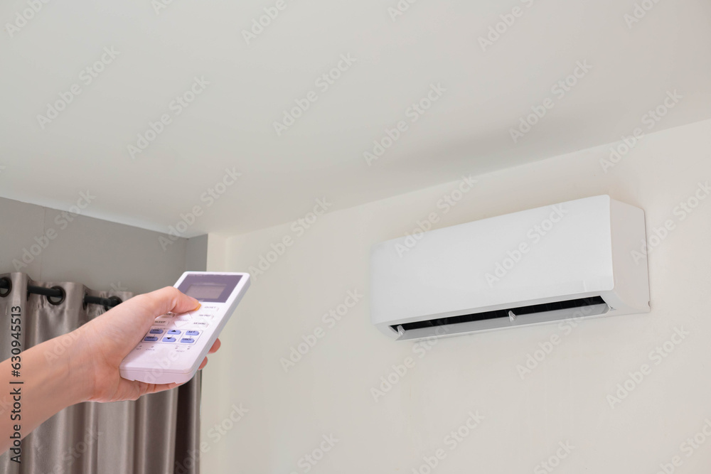 Fototapeta premium Hand pressing remote control air conditioner in room.