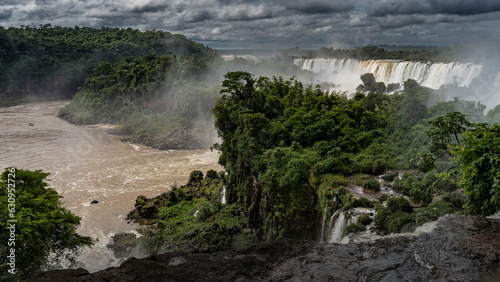 Waterfall landscape. Iguazu Falls cascade with spray and fog, stormy river, tropical green vegetation. Clouds in the sky. Argentina.