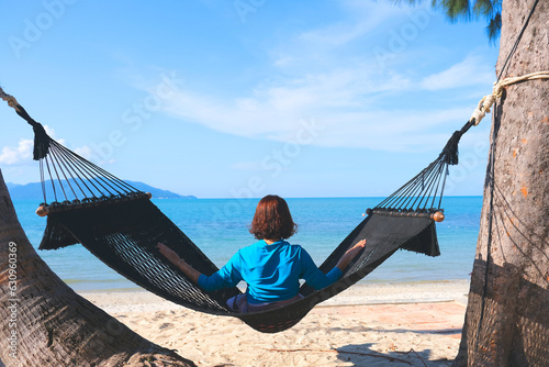 woman resting looking at the sea and mountains She sits in a hammock on a tropical beach. Beautiful tourism concept on the island.
