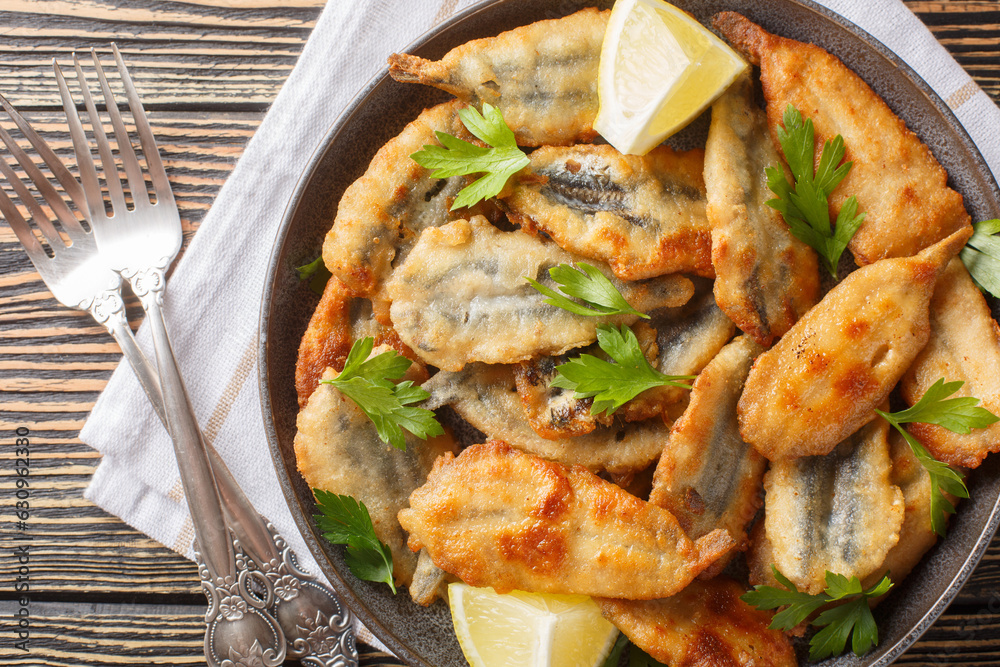 Fried breaded anchovy fillets served with lemon and herbs close-up on a plate on the table. Horizontal top view from above Fried breaded anchovy fillets served with lemon and herbs close-up on a plate on the table. Horizontal top view from above