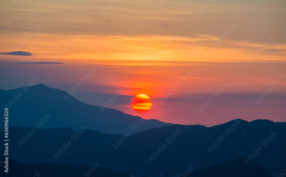 The orange-red sunset is covered by clouds as it moves towards the horizon. View of the urban landscape from Dajianshan Mountain, New Taipei City, Taiwan