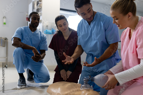 Biracial male doctor with diverse trainee doctors learning cpr on model at hospital