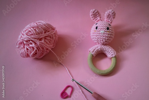 Crocheted Pink Bunny rattle with cotton yarn and neele hook isolated on pink background. Craft concept. Baby toy handmade. Pink knitted rabbit for children. Handmade rattle toy for newborn baby. photo