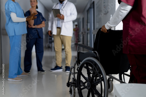 African american female doctor walking with wheelchair in corridor at hospital