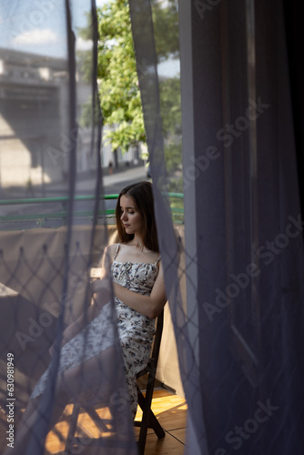 Girl through the curtains posing on the balcony in a white dress © Cavan