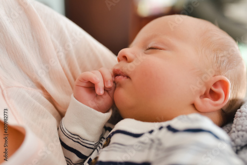 Newborn baby boy sleeping in his mother's arms at home