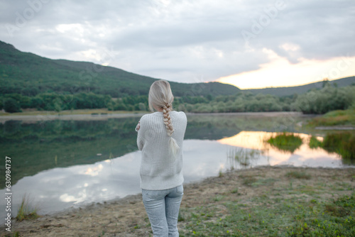 Back view of the blond woman dressed sweater and jeans., Walking in the shore of the lake with beautiful landskape. The girl enjoy the nature  in her trip © Вероника Зеленина