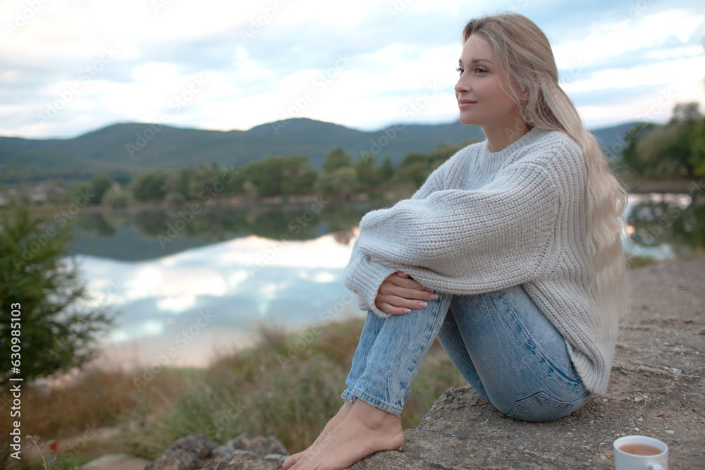 The blond woman dressed sweater and jeans., Walking in the shore of the lake with beautiful landskape. The girl enjoy the nature in her trip The blond woman dressed sweater and jeans., Walking in the shore of the lake with beautiful landskape. The girl enjoy the nature in her trip