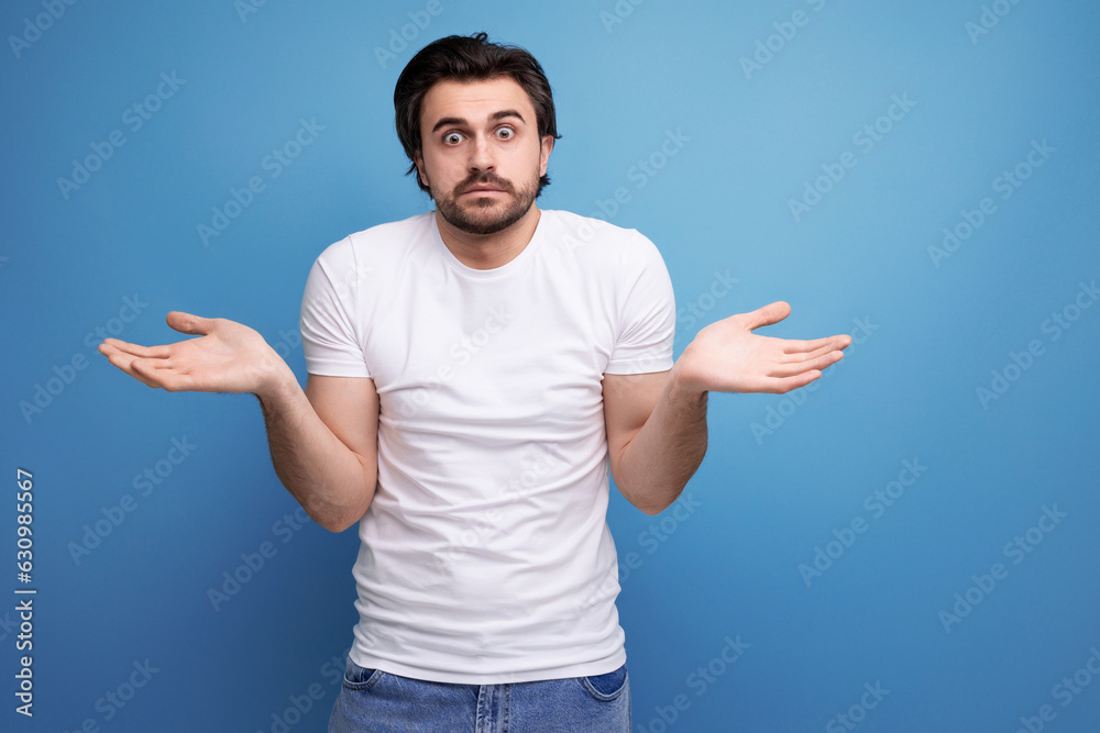 bearded brunette guy in white t-shirt shows refusal gesture on studio background with copy space bearded brunette guy in white t-shirt shows refusal gesture on studio background with copy space