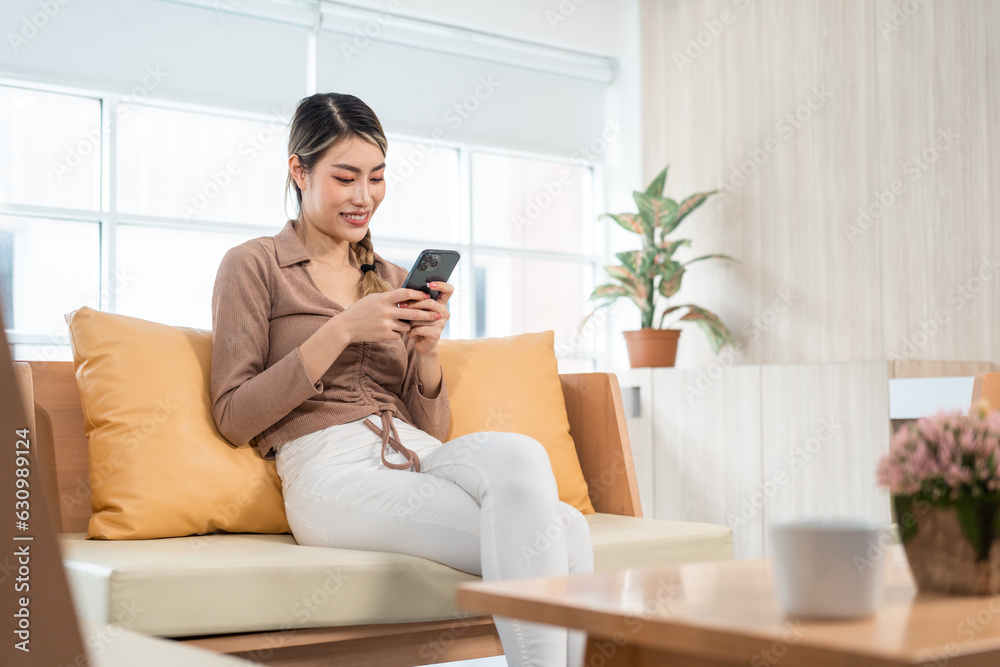 Beautiful young women using mobile phone sitting on sofa in living room. Using smartphone. Woman Shopping online store. Relax time at home Beautiful young women using mobile phone sitting on sofa in living room. Using smartphone. Woman Shopping online store. Relax time at home