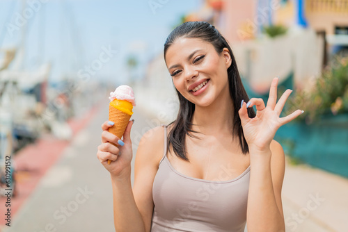 Young pretty woman with a cornet ice cream at outdoors showing ok sign with fingers