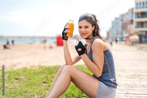 Young pretty sport woman holding an orange juice at outdoors and pointing it