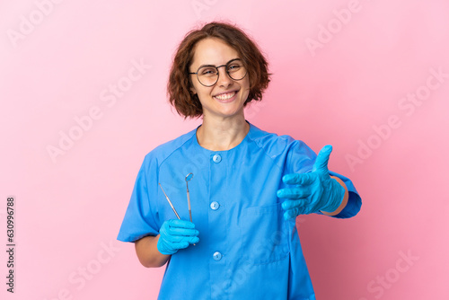 Woman English dentist holding tools over isolated on pink background shaking hands for closing a good deal