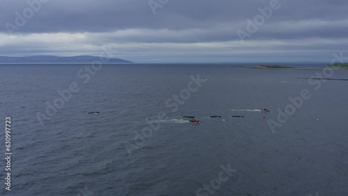 Sideview aerial of currach boat canoes paddling in open ocean with support vessel near by photo