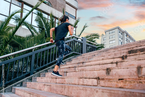 Unrecognizable young female runner training up stairs in urban runway with palm trees on sunset