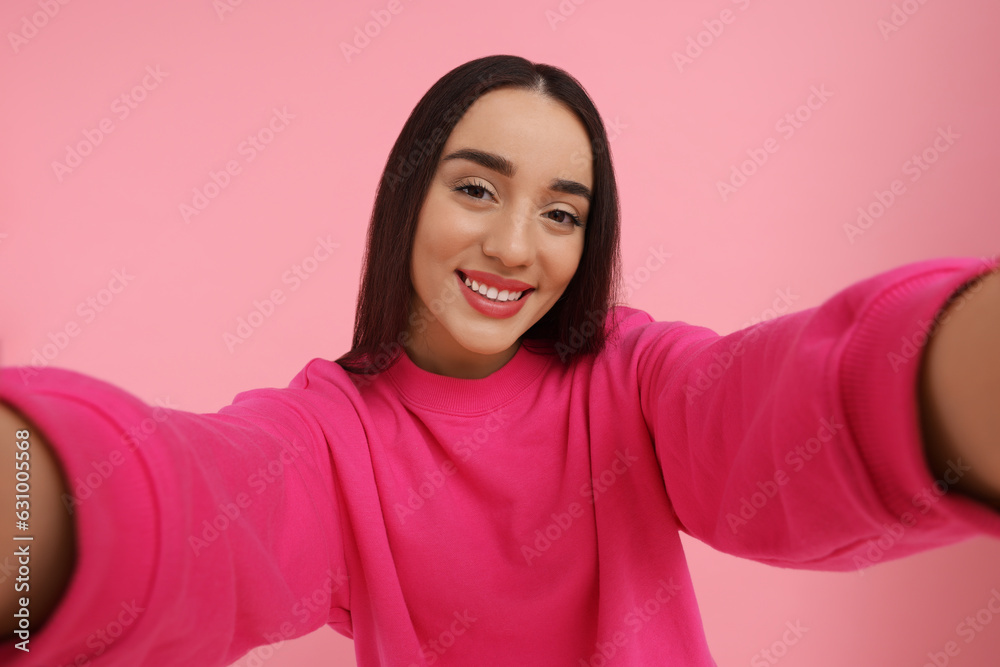 Smiling young woman taking selfie on pink background Smiling young woman taking selfie on pink background