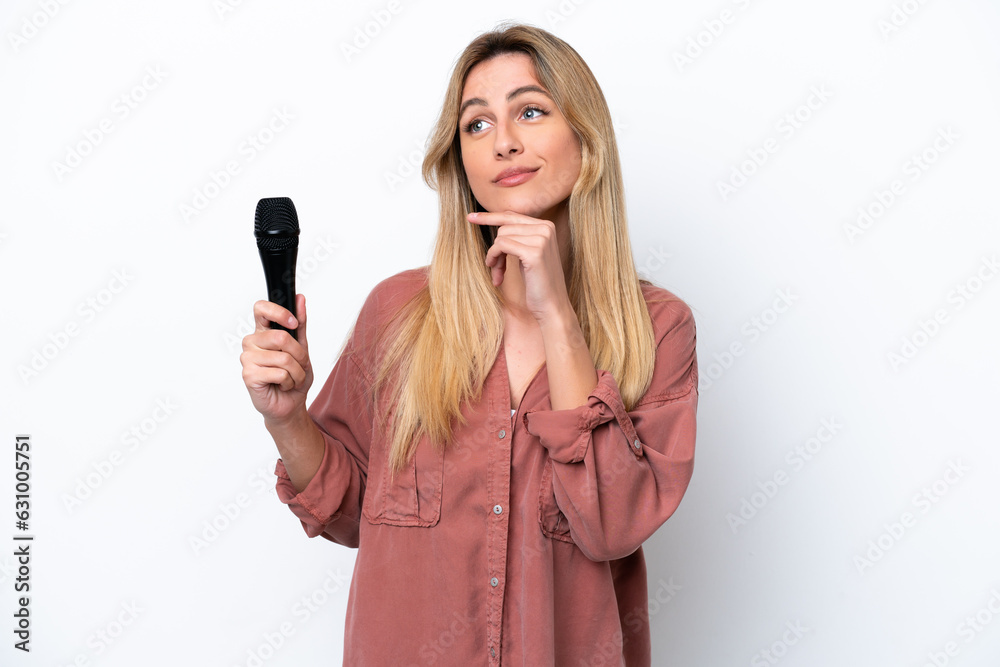Singer Uruguayan woman picking up a microphone isolated on white background having doubts while looking up Singer Uruguayan woman picking up a microphone isolated on white background having doubts while looking up