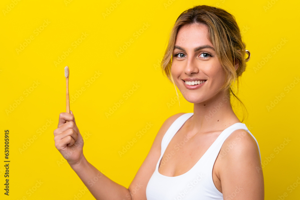 Young Uruguayan woman brushing teeth isolated on yellow background smiling a lot Young Uruguayan woman brushing teeth isolated on yellow background smiling a lot
