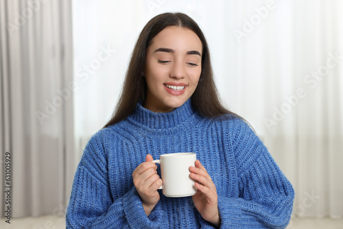 Happy young woman holding white ceramic mug at home