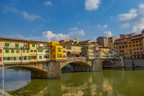 Famous medieval bridge Vecchio through Arno river with jewelry and souvenir shops in Florence, Italy, at sunny day and blue sky